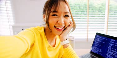 A young adult woman working from home, joyfully using her phone to create content; illustrating the 'always-on' digital lifestyle of Gen Z that creates friction with traditional Boomer workplace expectations.