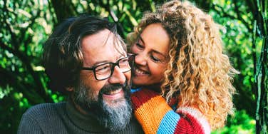A happy couple in their young-mature years embracing outdoors against a lush green background; illustrating the friendship and deep-seated loyalty found in high-quality, long-term relationships.
