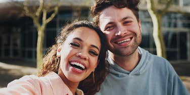 A smiling man and woman capturing a joyful moment on a university campus; illustrating the proactive 'memory-making' habits that keep emotionally secure couples grounded and connected during dry spells in their relationship.