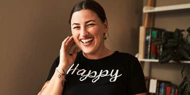 A portrait of a happy woman smiling with pride while lounging at home, showcasing her tattoos and natural beauty; illustrating the practice of being 'fully oneself' and finding comfort in one's own skin.