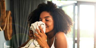 A Black female person smelling a sweater in a sunlit home; illustrating the science-backed habit of using familiar, clean domestic scents to regulate the nervous system and reduce stress.