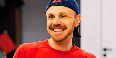 A man smiling intently at the camera in a vibrant red shirt; illustrating the 'appeasement' behavior that can signal a lack of internal boundaries and reliability in a professional or personal setting.