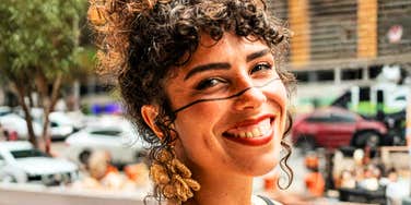 A portrait of a woman with stylized curly hair and gold earrings; illustrating the 'status signaling' and fixation on outward appearances that can indicate a person cares too much about surface-level social markers.