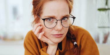 A close-up portrait of a pensive woman in glasses resting her chin on her hand; illustrating the analytical focus required to identify the deep-seated psychological divides in generational parenting.