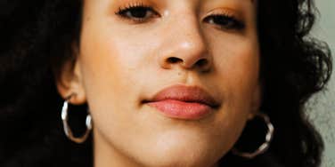 A woman showing a clear view of her ear and temple area while wearing silver hoop earrings; illustrating the 'vestigial' trait that some scientists believe is an evolutionary link to fish gills.