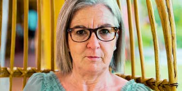 A senior woman wearing glasses and a teal lace top sitting in a relaxed garden setting; illustrating the 'traditional principles' of the 1950s and 60s, such as lifelong institutional loyalty and formal social hierarchies, that have shifted in the modern era.