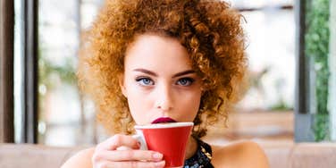 A woman holding a coffee cup with a pensive but intense expression in her eyes; illustrating the 'mask of normalcy' and the quiet, observant traits used by manipulative individuals to gather information and influence others.