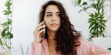 A portrait of a woman in professional pink attire looking focused while on a call; illustrating the non-verbal cues and 'soft power' strategies a career coach recommends for handling workplace rudeness.