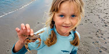 An authentic photo of a young girl at the seashore, looking happy and proud as she holds a crab; illustrating the author's belief in reinforcing a daughter's self-worth and beauty regardless of expert opinions.