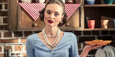 A woman dressed as a traditional 1950s housewife holding baked goods; illustrating the highly stylized and curated nature of the 'tradwife' movement that flourished and then faded on social media.