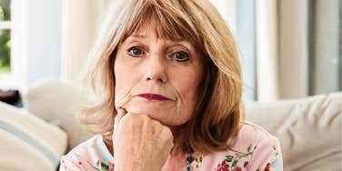 A portrait of a senior woman on a sofa appearing anxious and suffering from depression; illustrating the generational divide in how stress is managed and the critique of the 'panic' response in older adults.