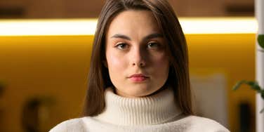 A calm but intense female headshot in a living room setting; illustrating the analytical and somewhat somber realization of how Millennial behaviors were shaped by the expectations of their Boomer parents.