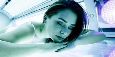 A woman using a tanning bed at a salon; illustrating the direct link between artificial UV exposure and the risk of developing significant skin health issues, including carcinoma.
