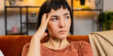 A depressed woman looking pensive and distressed while sitting alone in a living room; illustrating the internal turmoil and 'unfair situation' of a woman harboring a lie she intends to take to her grave.