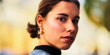 A portrait of a woman looking back with a steady, self-assured gaze; illustrating the non-reactive body language and verbal boundaries used by resilient individuals when faced with disrespect.