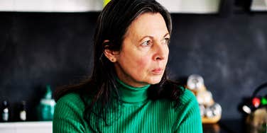 A frustrated woman looking around her kitchen; illustrating the psychological drive to control one's immediate environment through remodeling when the outside world feels increasingly unstable.