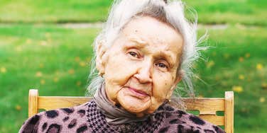 A mature woman sharing a serene, direct gaze from a lush green garden setting; illustrating 'mindful longevity' and the quiet, internal coping mechanisms that foster emotional connection and late-life serenity.