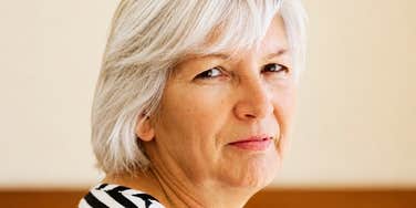 A close-up lifestyle portrait of a mature woman sitting in a quiet home environment with a somber expression; illustrating 'the proximity pressure matrix' where domestic expectations fuel geographic separation