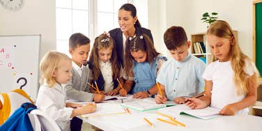 teacher standing around group of students writing 