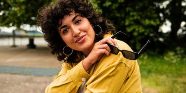 talented gen z woman smiling holding her sunglasses