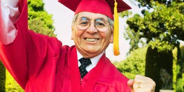Portrait of an excited senior man in graduation attire holding degree
