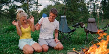 man swatting at a mosquito on his girlfriend's leg while camping