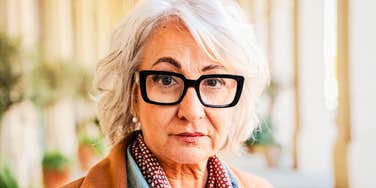 A classic portrait of a strong, mature female relative looking forward with a serious, discerning gaze; illustrating the defense of maternal choice and the confrontation of parental double standards within modern families.