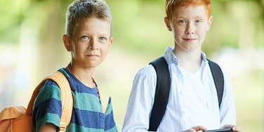 Two tween boys with backpacks, one using a phone 