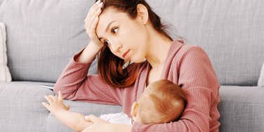 A tired mother sitting, breastfeeding her infant baby; a visual representation of the exhausting reality behind workplace pregnancy discrimination.
