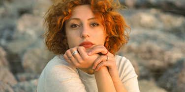A close-up portrait of a serious, red-haired woman with a neutral, introspective expression; illustrating 'relational caution' and the behavioral barriers that impact social bonding.