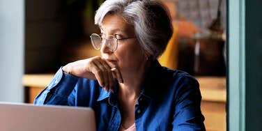 A close-up portrait of a senior professional woman focused on her computer screen inside a modern workspace; illustrating 'the generational ceiling effect' where older demographics retain leadership roles.