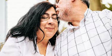 A tender lifestyle shot of a husband kissing his wife's forehead; illustrating 'the affirmation loop model' where mutual safety and regular affection serve as foundations for a thriving marriage.