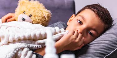 A young boy sitting on a couch with a teddy bear; a visual representation of 'the vulnerable dependent' whose severe medical celiac disease boundaries were deliberately crossed by a grandparent.