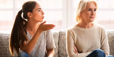 A close-up lifestyle shot of a tense conversation between an older mother with a defensive posture and her adult daughter; illustrating 'the generational gatekeeping model' where a gap in child safety standards triggers a family rift.