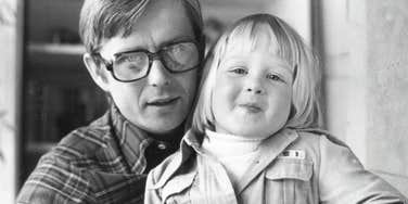 A vintage 1970s black and white photo of a father and his young daughter laughing together on wooden steps while playing with a toy boat; representing 'unplugged engagement' and the old-fashioned parenting habits that build deep emotional connections.