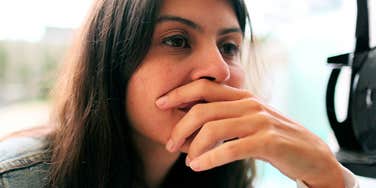 A close-up portrait of an anxious, introspective woman lost in deep thought against a minimalist backdrop; illustrating 'the relational hypervigilance framework' where childhood isolation causes chronic adult overthinking.
