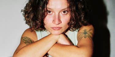 A close-up portrait of a woman with a neutral face resting on her arms; illustrating 'evolutionary signaling theory' and the non-obvious physical or behavioral traits that biological anthropologists say trigger instant social evaluations.