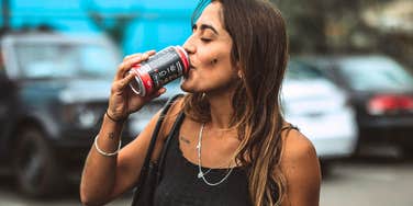 A woman holding a aluminum can and taking a drink of a popular carbonated beverage; illustrating the routine consumption patterns evaluated in recent medical research regarding stroke risk.