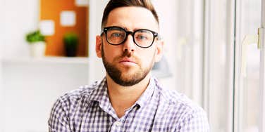 A casual employee sitting at an office desk with a neutral, un-engaged expression; a visual representation of 'the cloaked disengagement' and the growing corporate frustration surrounding Pistachio Leadership.