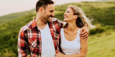 A young man and woman sharing a tender, smiling moment outdoors surrounded by green spring foliage; illustrating healthy emotional regulation that prevent fight before they start