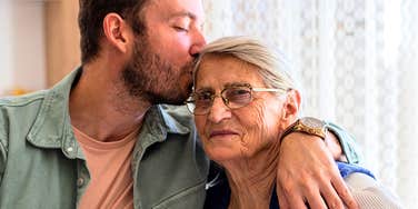 adult child giving his older mom a kiss on the forehead 