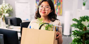 A close-up portrait of an elegant woman in smart clothing and glasses leaving her workspace with a box of personal belongings; illustrating 'the career autonomy pivot' and modern shifts in how different generations define professional success.