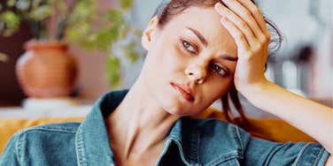 A close-up portrait of an anxious woman on a sofa, looking overwhelmed by a message on her smartphone screen; illustrating 'role reversal anxiety' and the mental load of managing aging parents' technical and emotional needs.