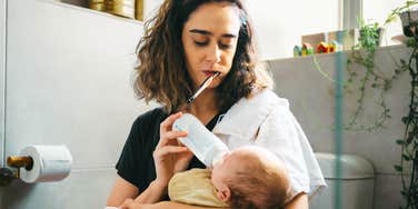 A close-up lifestyle shot of an exhausted woman managing childcare and basic personal hygiene at the same time; illustrating 'the cognitive overload conflict' where invisible household labor causes parental burnout.