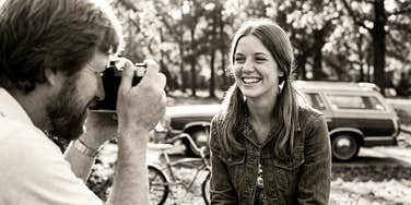 Woman laughing confidently while her partner photographs her, capturing the kind of thoughtful attention many women find meaningful in relationships