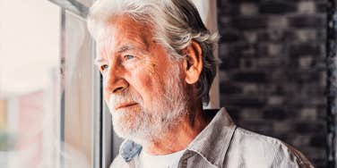 A close-up side profile of a mature, middle-aged grandfather lost in thought while looking through a window; illustrating a 'post-career recalibration' and the quiet introspection that comes with re-evaluating what really matters.