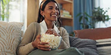 woman sitting on couch watching tv while eating popcorn