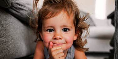 A curious young girl lying on the floor, smiling thoughtfully with her hand on her chin; a visual representation of 'the incipient intellect' and early cognitive traits tied to genetic inheritance.