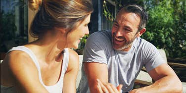 An outdoor photograph of a mature husband and wife chatting comfortably on their house porch, illustrating high emotional safety, active listening, and relationship longevity.