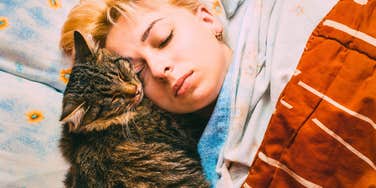 happy woman sleeping in bed with her cat nuzzled against her face